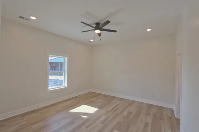 an empty room with wooden floor ceiling fan and windows