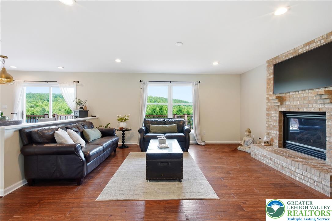 115 West Butternut Road Hellertown, PA 18055 - Photo 25 of 97 Hardwood flooring extends throughout this well-lit living area, featuring a brick fireplace and abundant natural light from large windows.