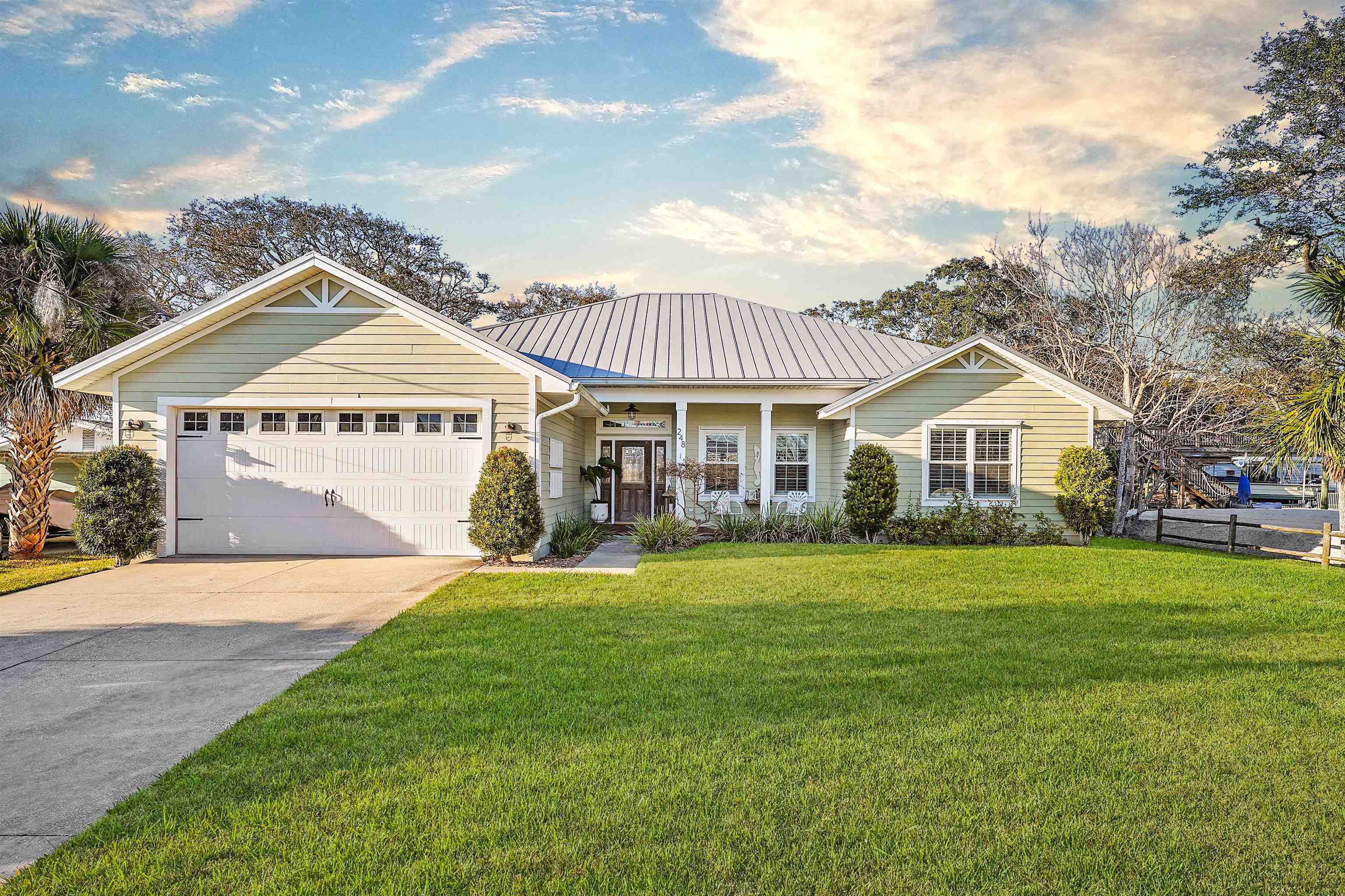 View of front facade with driveway, covered porch, a garage, and a metal roof