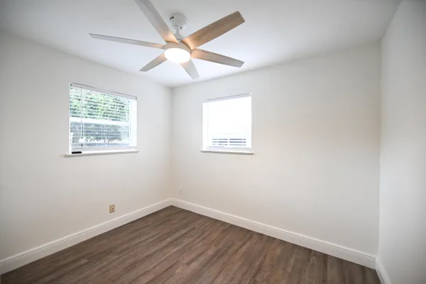 an empty room with wooden floor ceiling fan and windows