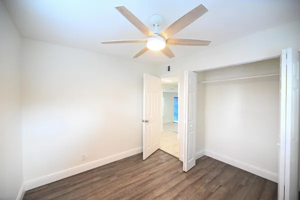 an empty room with wooden floor fan and windows