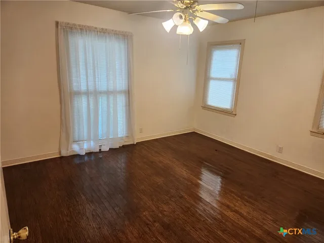 an empty room with wooden floor fan and windows