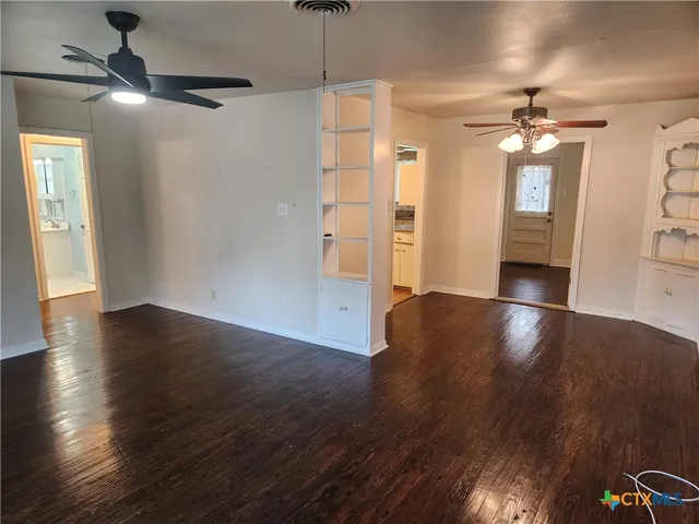 a view of a livingroom with wooden floor a ceiling fan and windows