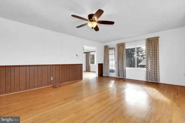 a view of an empty room with wooden floor and a ceiling fan