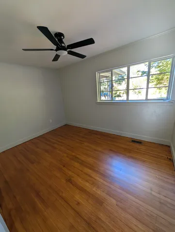 an empty room with wooden floor fan and windows