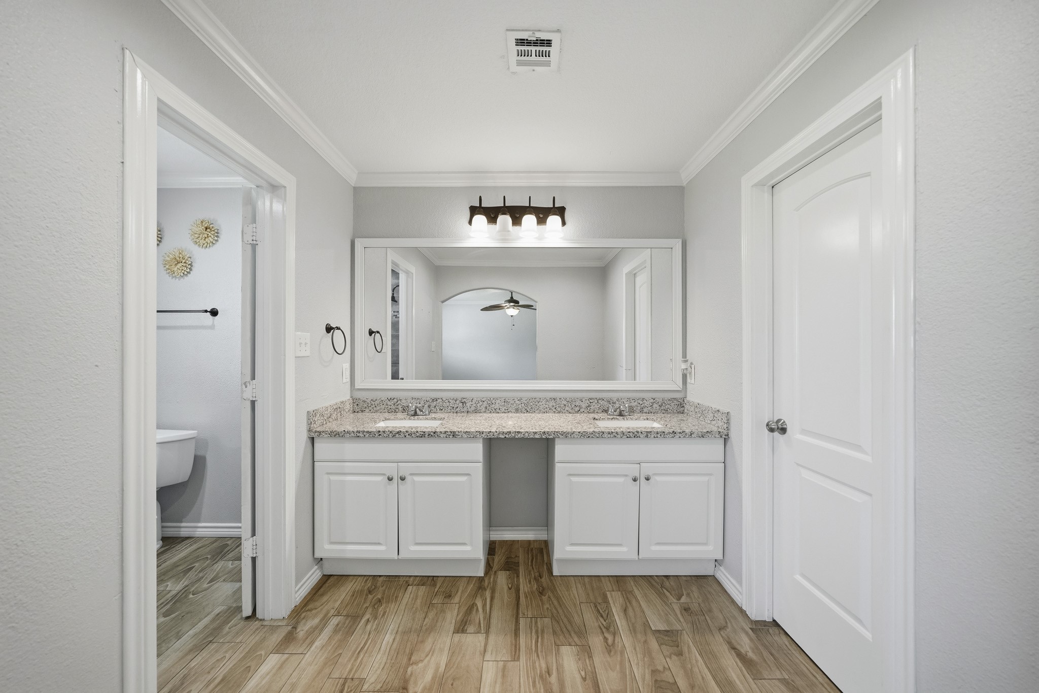 302 Country Road 893 Angleton, TX 77515 - Photo 21 of 26 This bathroom features a dual-sink vanity with granite countertops, white cabinetry, and wood-look tile flooring. It has a large mirror and modern lighting, with an adjacent toilet room for added privacy.