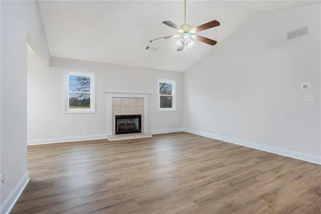 an empty room with wooden floor chandelier fan and windows