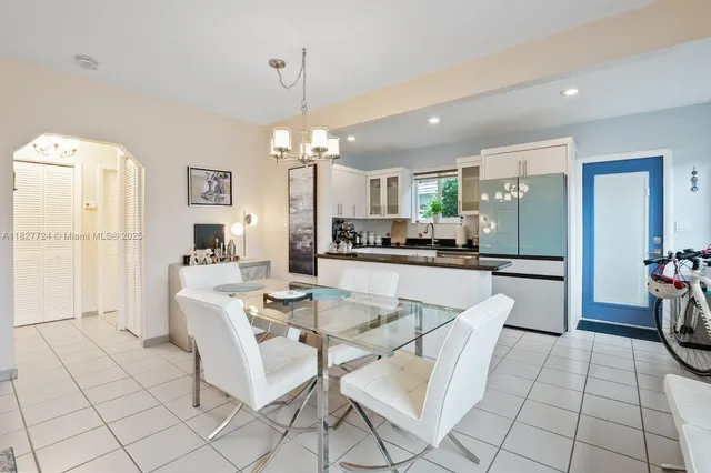 a dining hall with stainless steel appliances kitchen island granite countertop a dining table chairs and a refrigerator