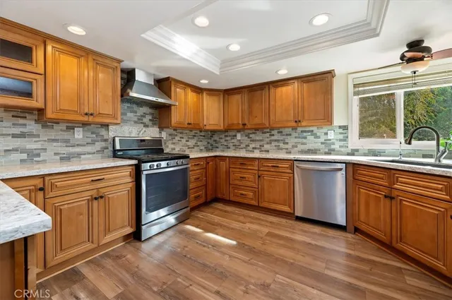 a kitchen with stainless steel appliances granite countertop wooden cabinets a sink a stove a refrigerator and island with wooden floor