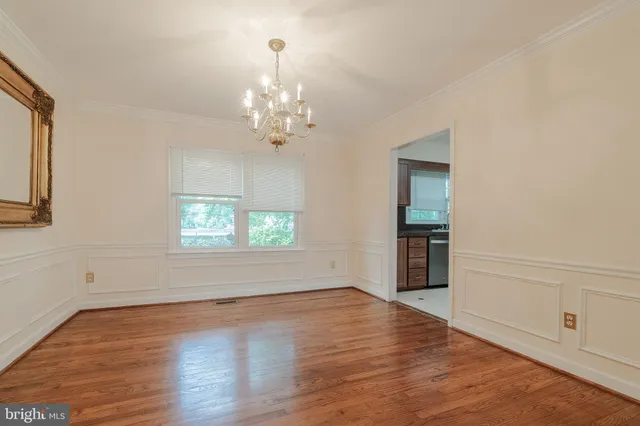 an empty room with wooden floor chandelier and windows
