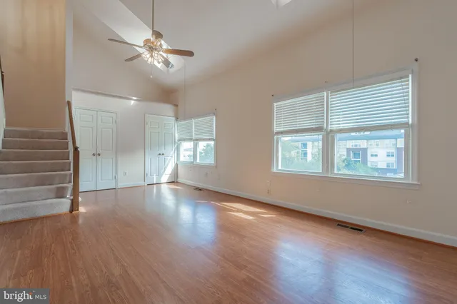 an empty room with wooden floor chandelier fan and windows