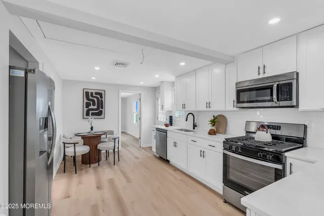 a kitchen with stainless steel appliances kitchen island granite countertop a stove top oven a sink a dining table and chairs with wooden floor