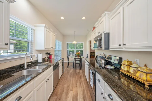 a kitchen with granite countertop a stove a sink a refrigerator dining table and chairs