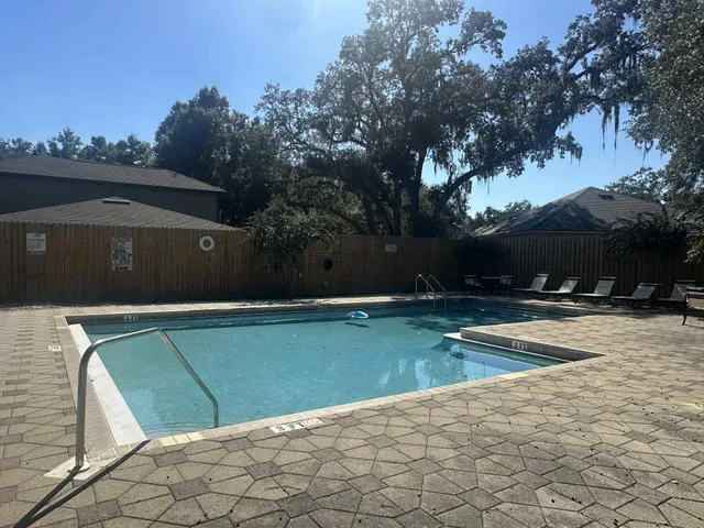 a view of swimming pool with lawn chairs and large trees