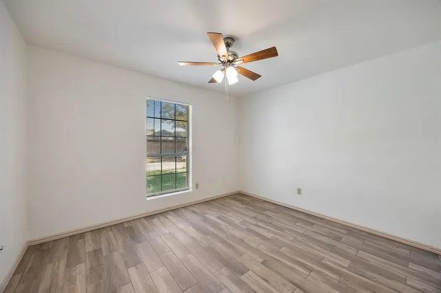 an empty room with wooden floor ceiling fan and windows