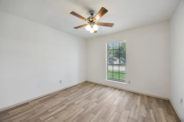 an empty room with wooden floor fan and windows