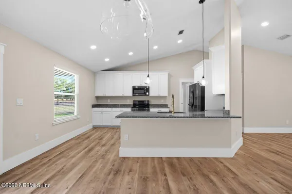 a view of kitchen with stainless steel appliances granite countertop wooden floors refrigerator and window