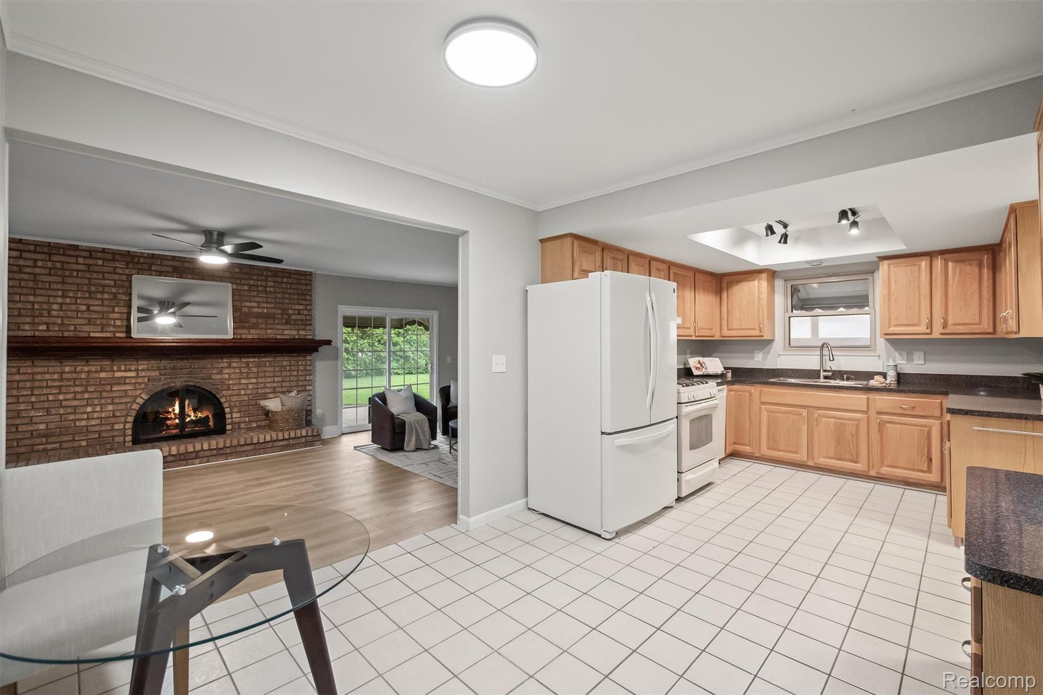 11326 Common Road Warren, MI 48093 - Photo 15 of 35 Kitchen with white appliances, light tile patterned floors, a brick fireplace, crown molding, and a ceiling fan