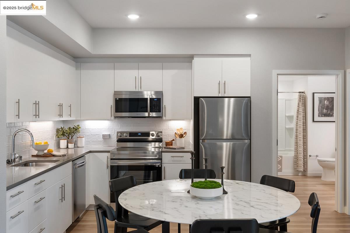 260 Brooklyn Basin Way, Unit 417 Oakland, CA 94606 - Photo 9 of 48 Kitchen featuring appliances with stainless steel finishes, backsplash, light wood-style flooring, white cabinetry, and dark stone counters