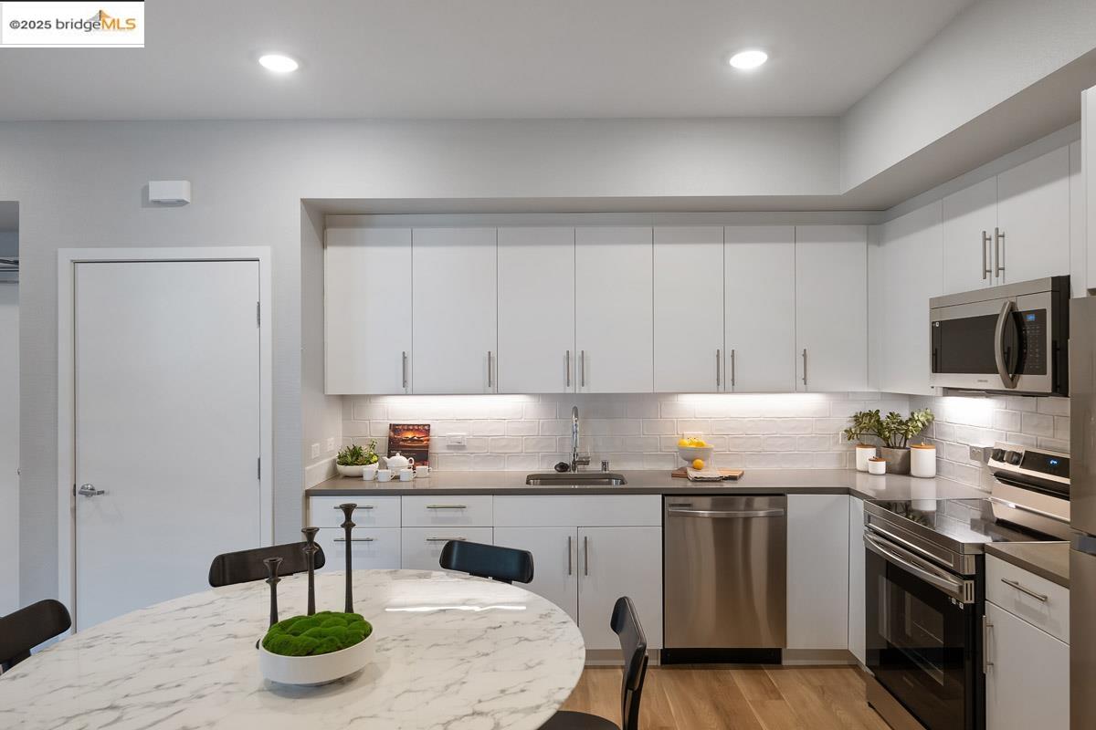 260 Brooklyn Basin Way, Unit 417 Oakland, CA 94606 - Photo 10 of 48 Kitchen with appliances with stainless steel finishes, white cabinets, light wood-type flooring, backsplash, and recessed lighting