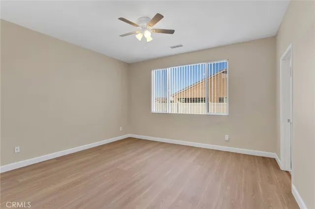 an empty room with wooden floor chandelier fan and windows