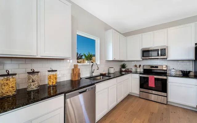 a kitchen with stainless steel appliances kitchen island granite countertop lots of white cabinets and wooden floor