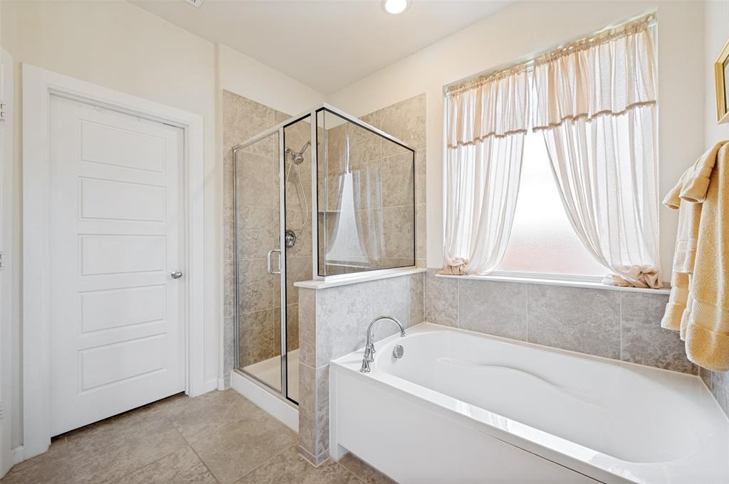 413 Wiggins Way Van Alstyne, TX 75495 - Photo 17 of 25 Bathroom featuring a white soaking tub with deck-mounted faucet, a separate glass-enclosed shower, light-colored wall tiles, and neutral floor tiles