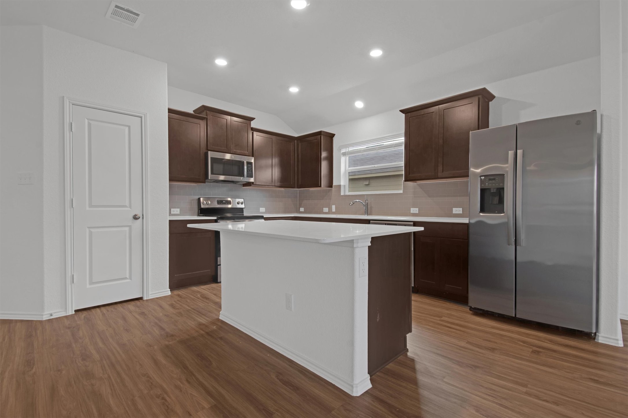 703 Bluejack Way Hutto, TX 78634 - Photo 9 of 19 Kitchen with stainless steel appliances, dark brown cabinetry, vaulted ceiling, decorative backsplash, and light wood-style flooring