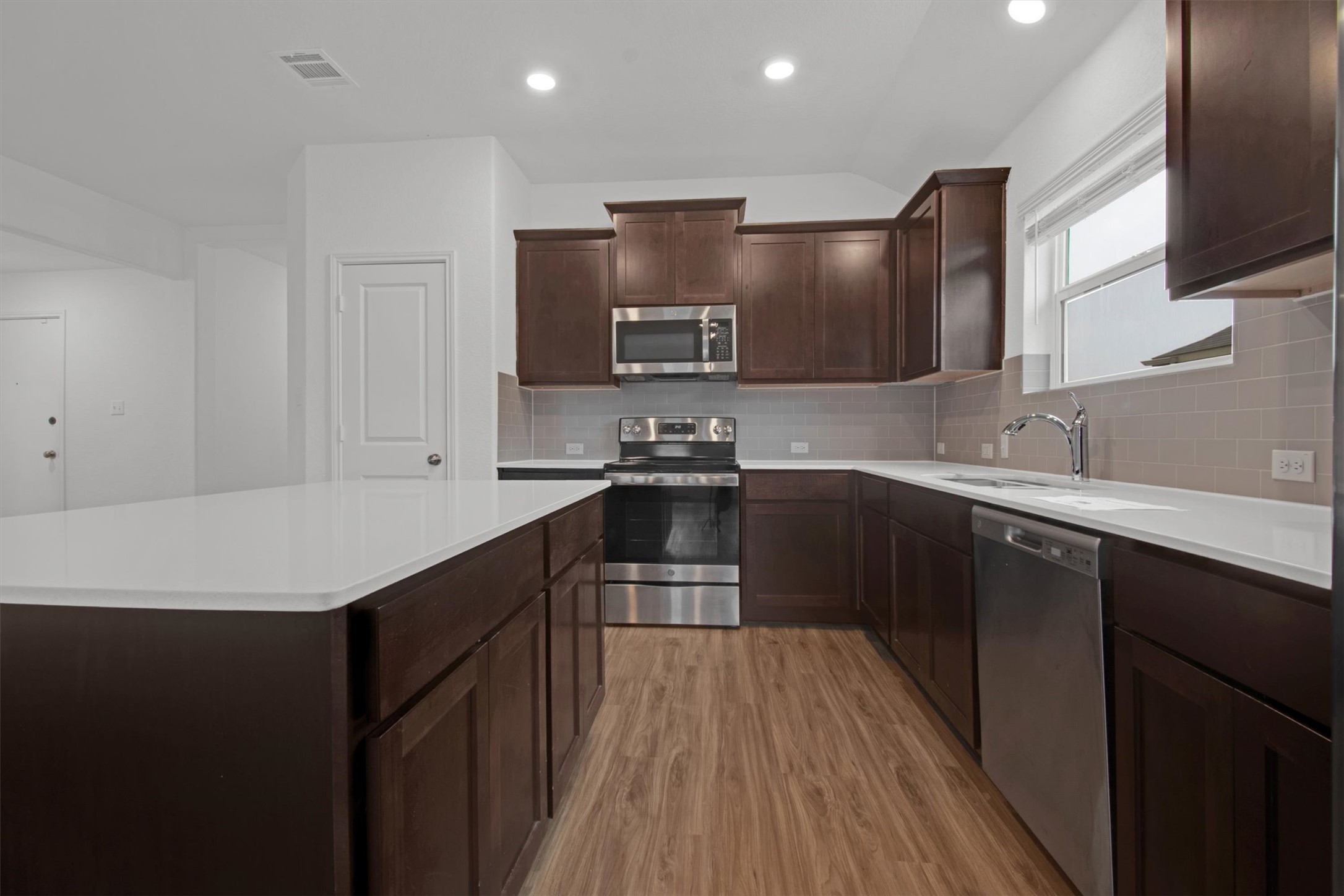 703 Bluejack Way Hutto, TX 78634 - Photo 10 of 19 Kitchen featuring appliances with stainless steel finishes, dark brown cabinetry, a kitchen island, light wood finished floors, and recessed lighting