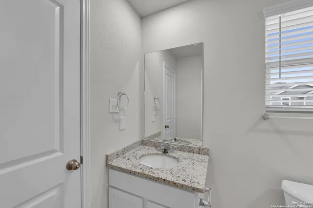 a bathroom with a granite countertop sink and mirror with toilet
