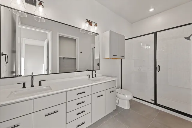 a spacious bathroom with double sink a toilet a mirror and shower