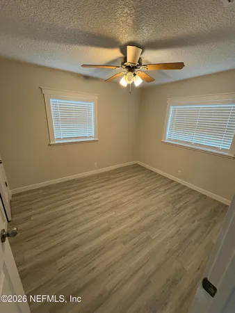 an empty room with wooden floor fan and windows