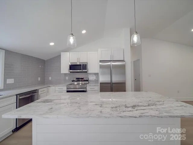 a large kitchen with a large counter top a sink stainless steel appliances and cabinets