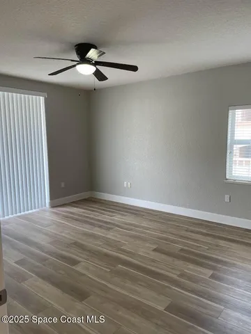 an empty room with wooden floor fan and windows