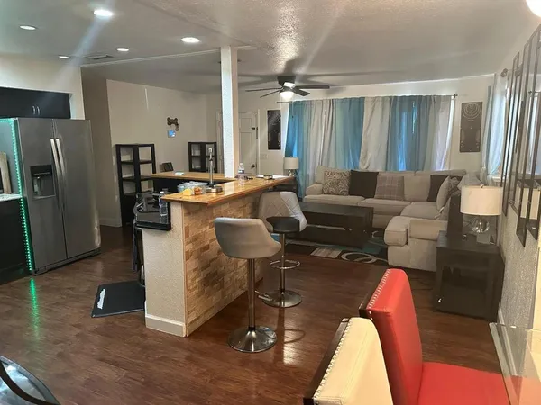 a living room with stainless steel appliances furniture a rug and a kitchen view