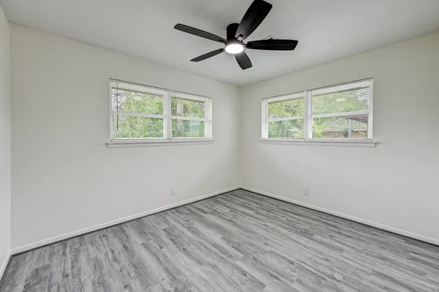 an empty room with wooden floor ceiling fan and windows