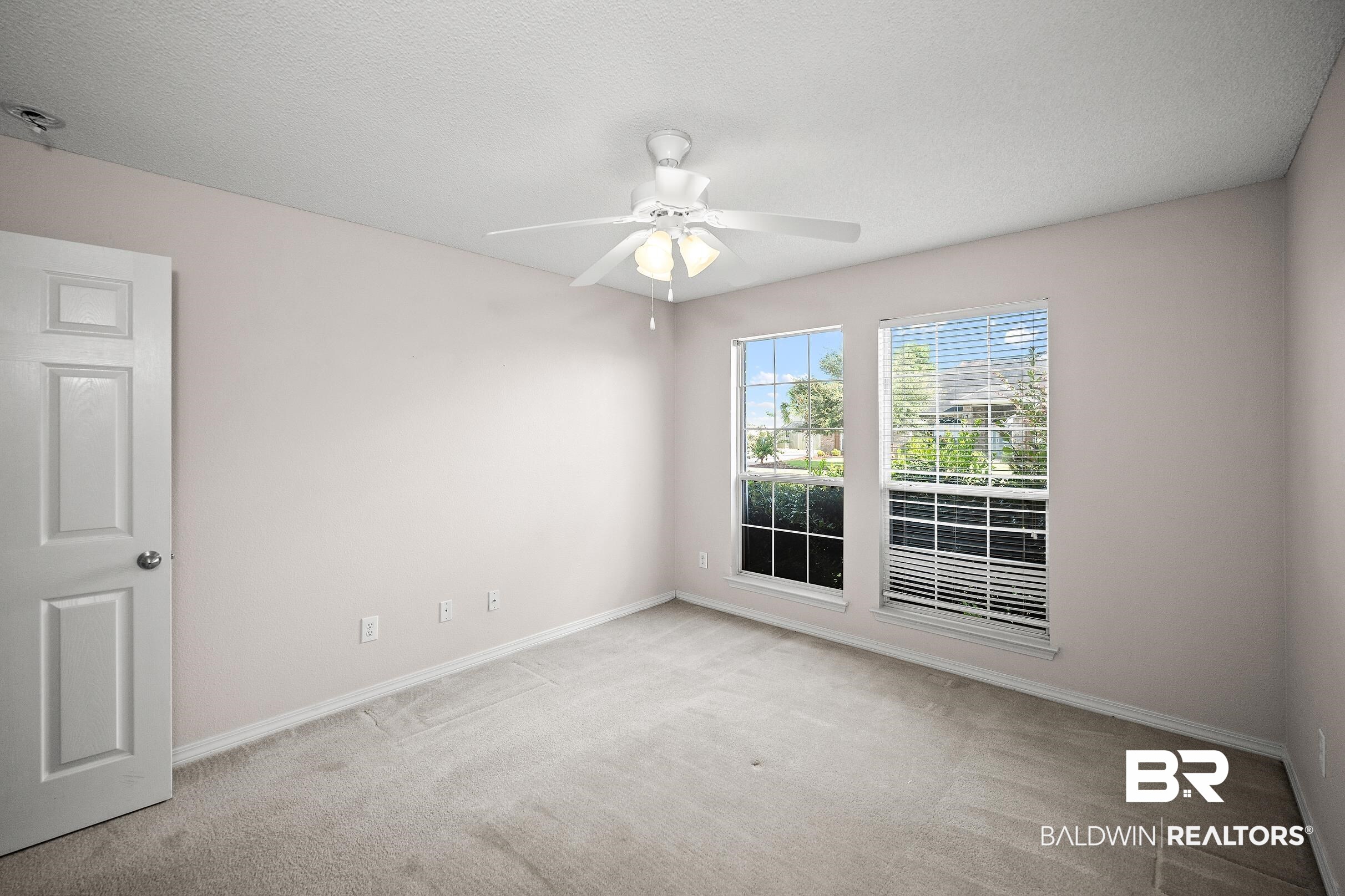 323 Manchester Lane Foley, AL 36535 - Photo 20 of 30 Expansive room featuring two windows with white blinds, neutral carpet flooring, and a ceiling fan with light fixture
