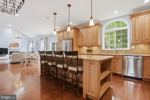 a open kitchen with granite countertop a stove a sink a dining table and chairs with wooden floor