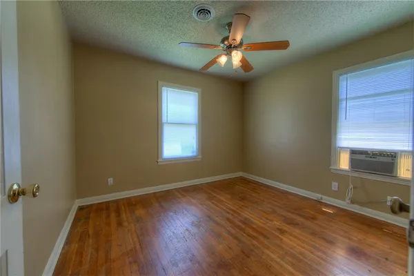 an empty room with wooden floor fan and windows