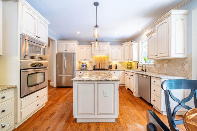 a kitchen with granite countertop a stove a sink dishwasher a refrigerator and white cabinets with wooden floor