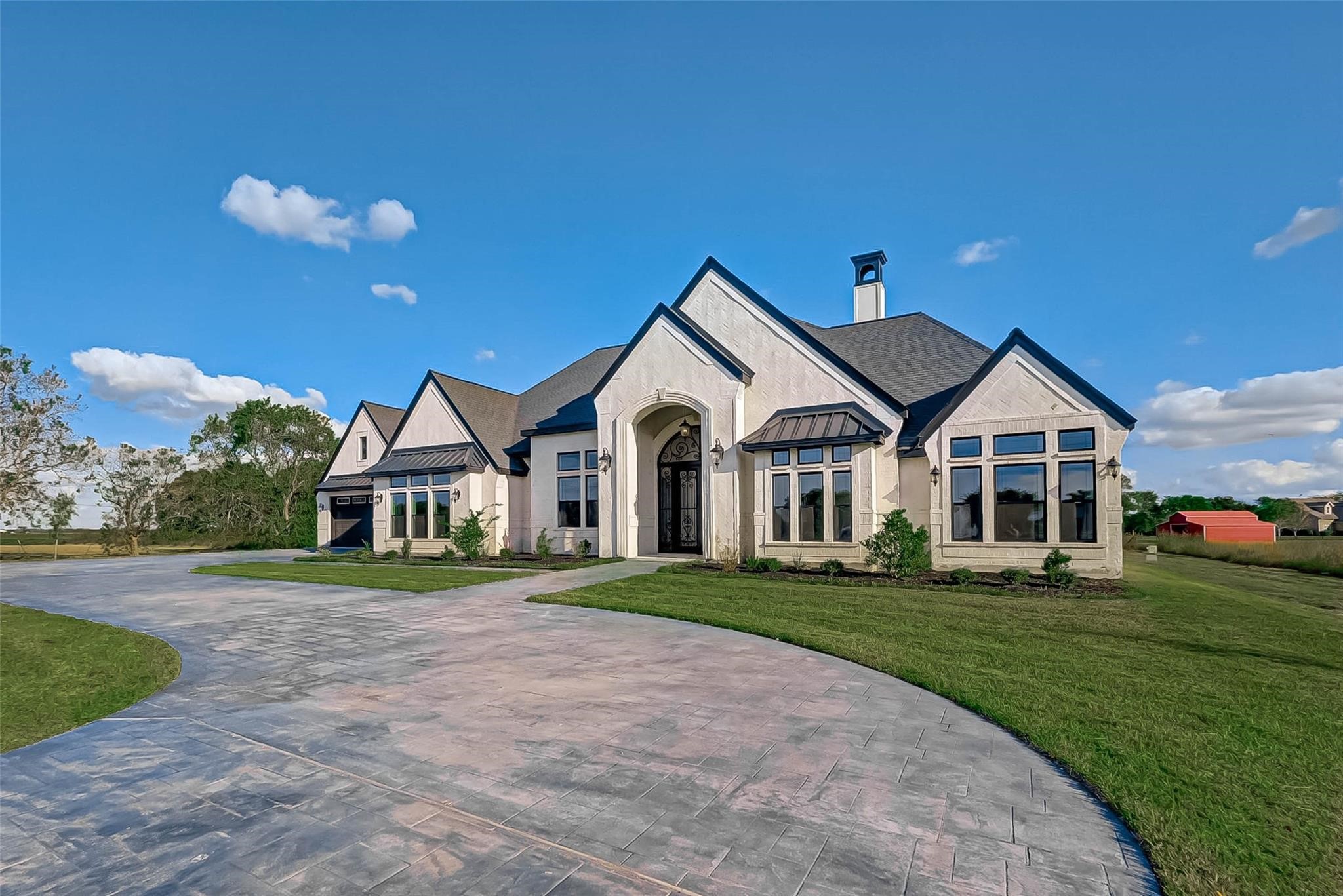 4821 Walters Road Richmond, TX 77469 - Photo 3 of 50 A stunning luxury estate showcasing modern European-inspired architecture with soaring rooflines, elegant stone and stucco finishes, and bold black trim accents. The expansive stamped concrete circular driveway creates a grand approach, leading to a dramatic arched entryway with custom iron front doors. Oversized windows flood the home with natural light while offering panoramic views of the surrounding acreage. The property exudes sophistication, privacy, and upscale country living.