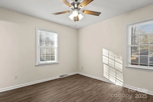 an empty room with wooden floor chandelier fan and windows
