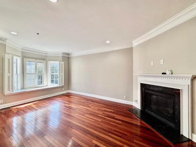 a view of an empty room with wooden floor fireplace and a window