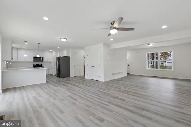 a view of an empty room with wooden floor and a kitchen
