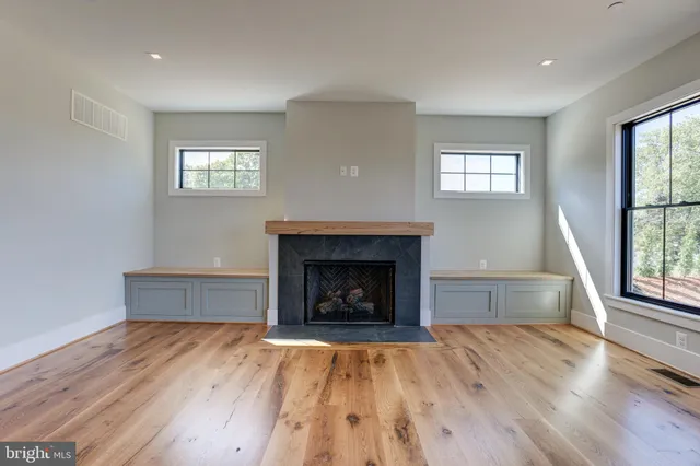an empty room with wooden floor fireplace and windows