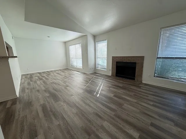an empty room with wooden floor fireplace and windows