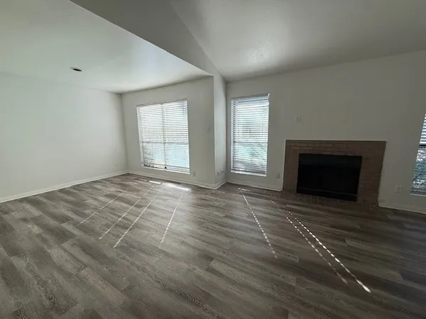 an empty room with wooden floor fireplace and windows