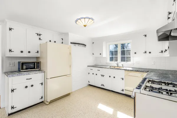 a kitchen with granite countertop a refrigerator stove a sink dishwasher and white cabinets with wooden floor
