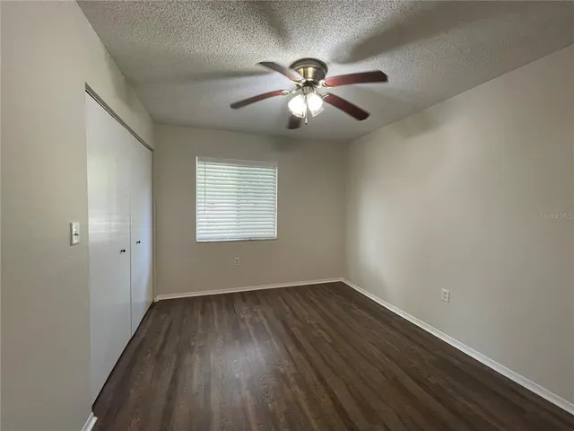 an empty room with wooden floor chandelier fan and windows