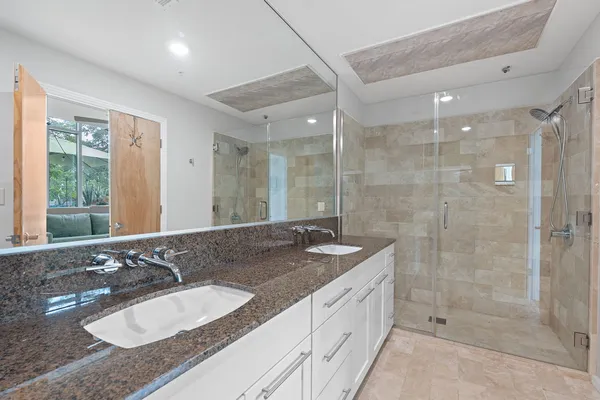 a bathroom with a granite countertop double vanity sink and shower